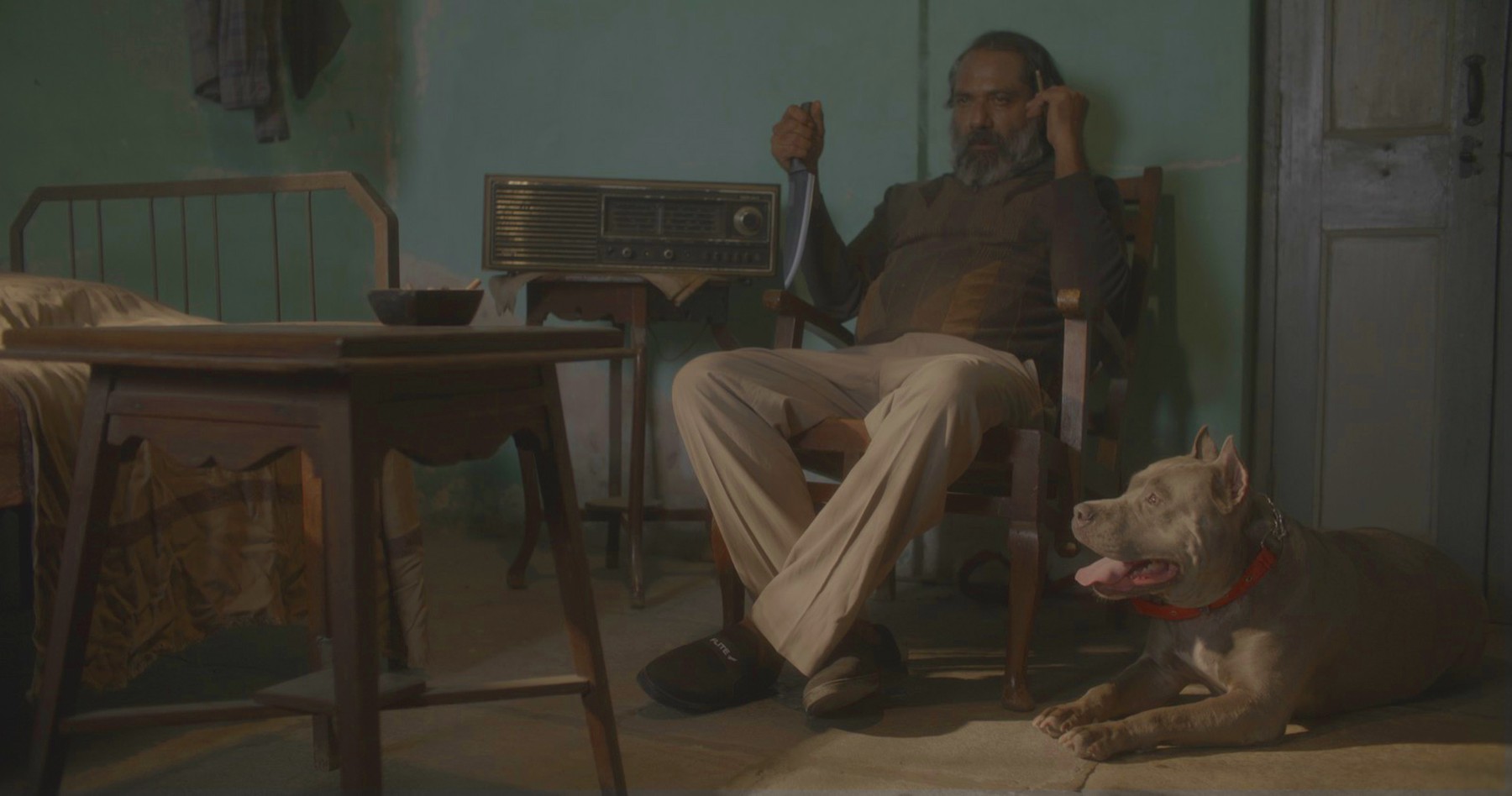 Man seated with a knife, dog beside him, still from Another Short Film About Killing