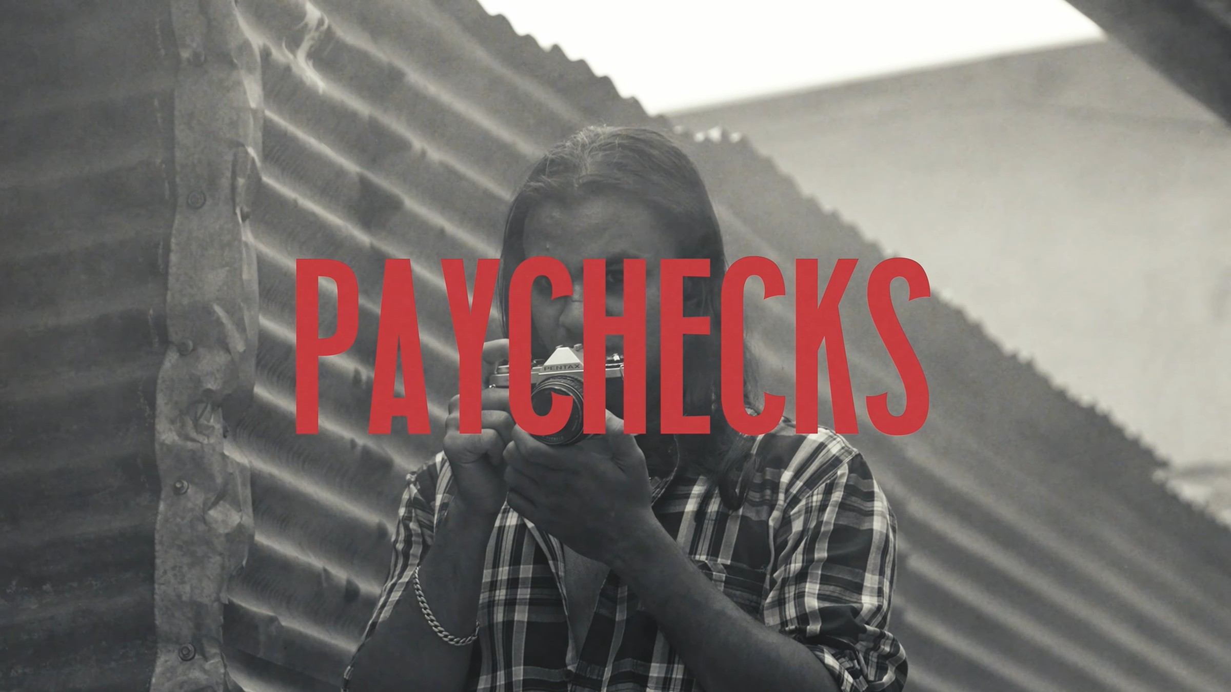 Paychecks title card, man photographing through a tin roof gap