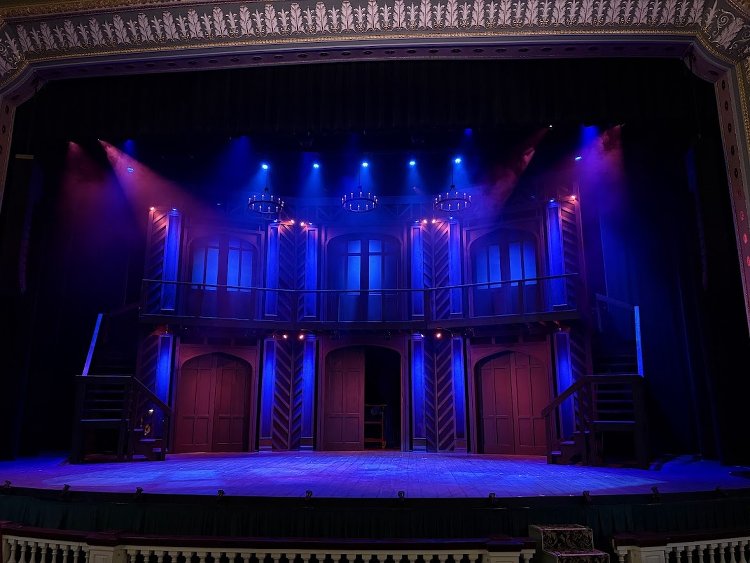 Empty Elizabethan two-storey stage set at the Lucas Theatre, lit in blue