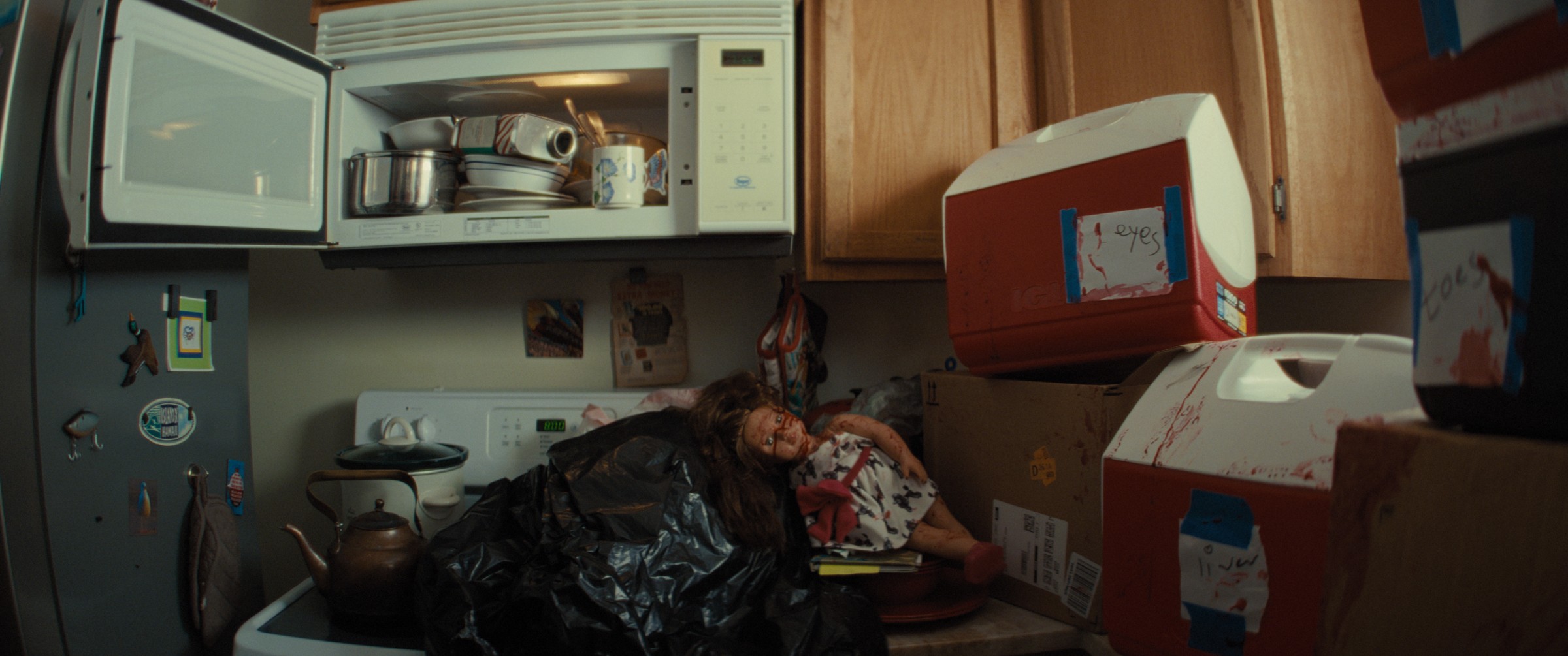 Doll in a trash bag amid coolers labeled with body parts, still from What Are Grandchildren Made Of?