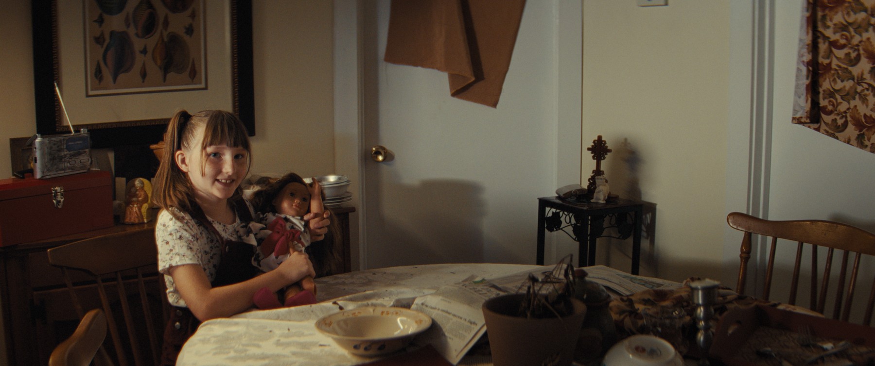 Girl smiling with a doll at the dining table, still from What Are Grandchildren Made Of?